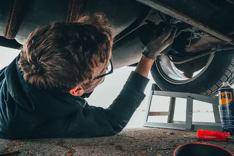 man under car doing auto repair, vehicle maintenance
