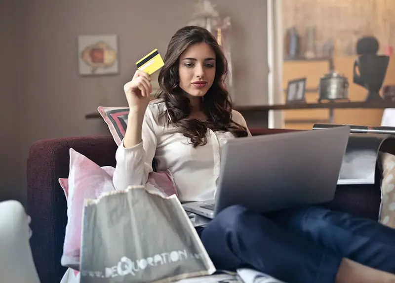 woman holding Visa card while using a silver laptop