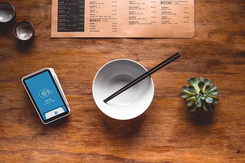 white ceramic bowl with chopsticks, nect to a plant and card reader
