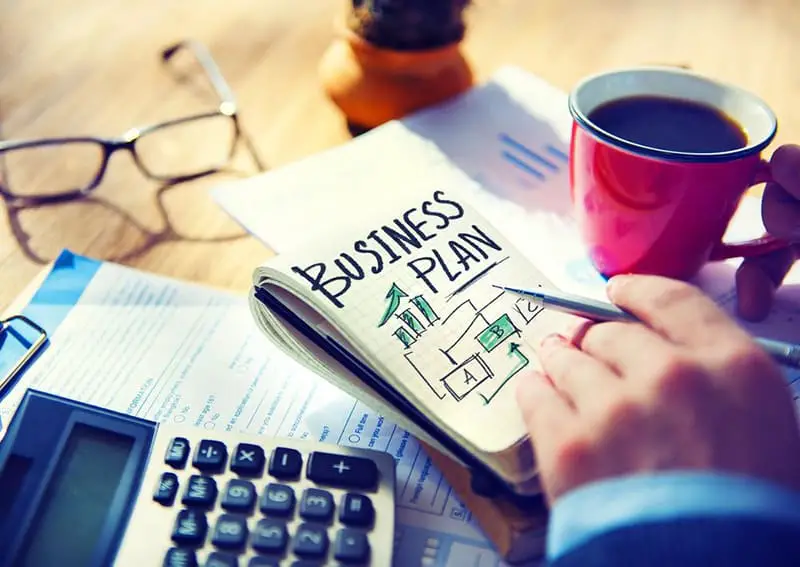 Person holding note book and cup of coffee creating a business plan