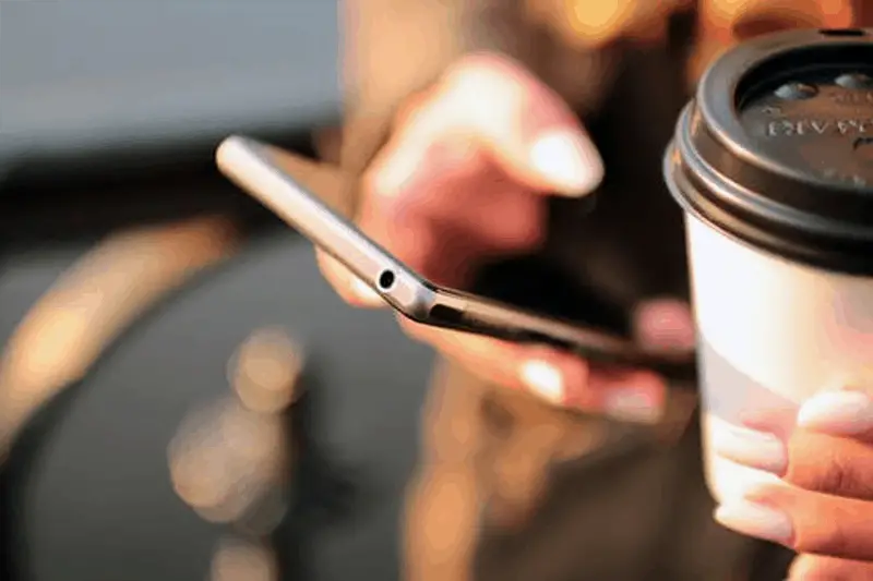 Person using mobile application and holding disposable coffee cup 