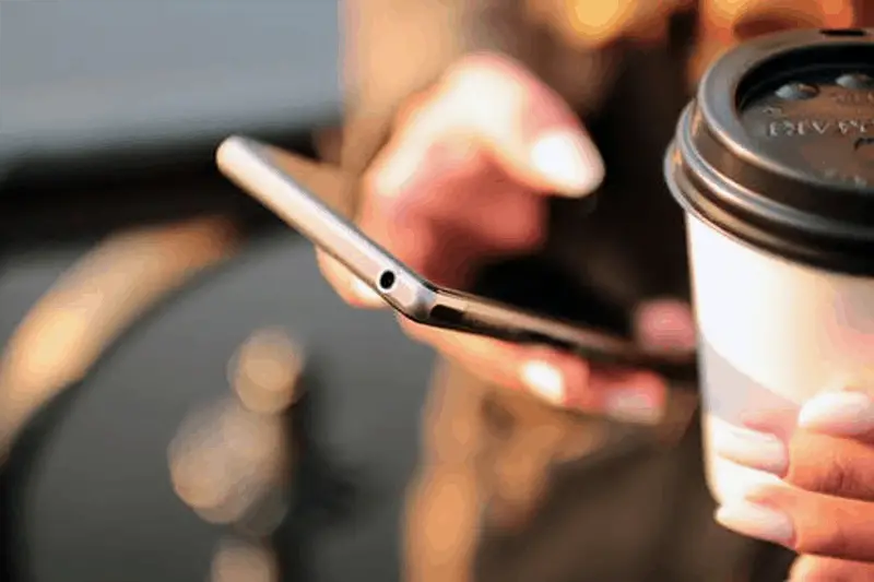 Person using mobile application and holding disposable coffee cup