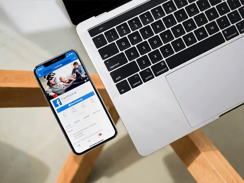 Mobile phone next to open laptop on glass table.