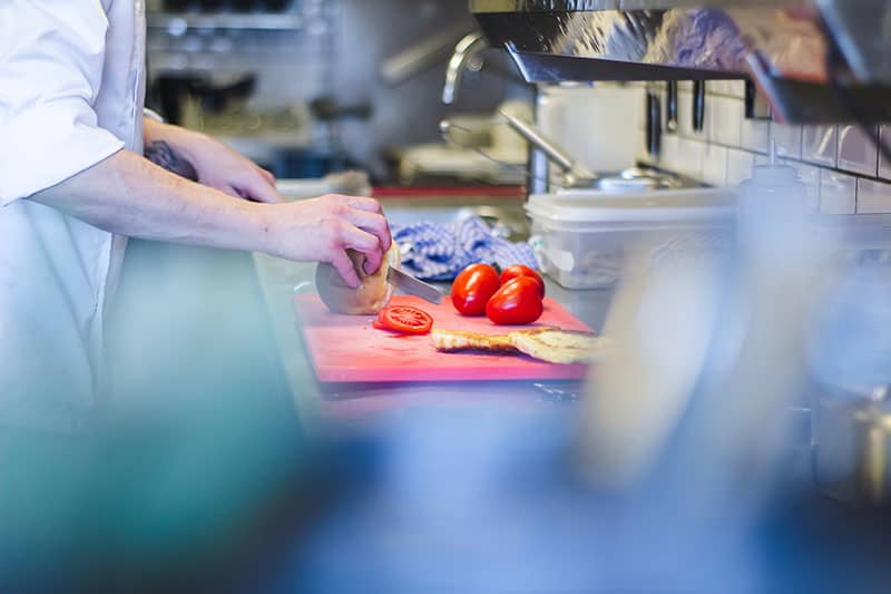 Chef slicing tomatoes and bread roll in a professional kitchen