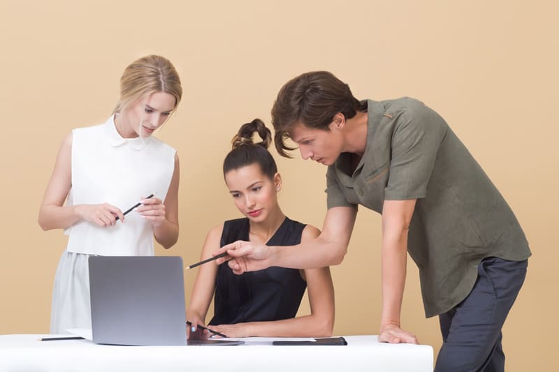 Two women and a man looking and pointing at a laptop