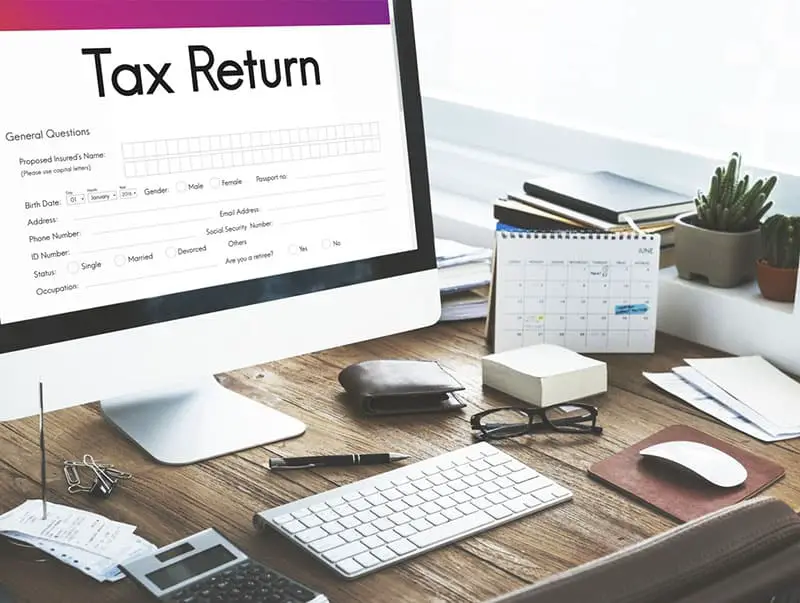 Tax return form on monitor screen on a desk with keyboard mouse calulator and other items