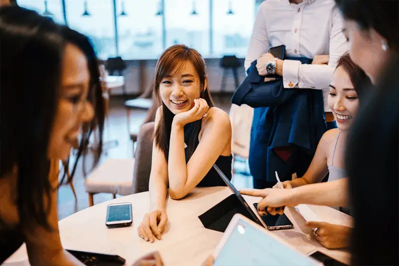 woman sitting on a grey chair in workplace surrounded by work colleagues