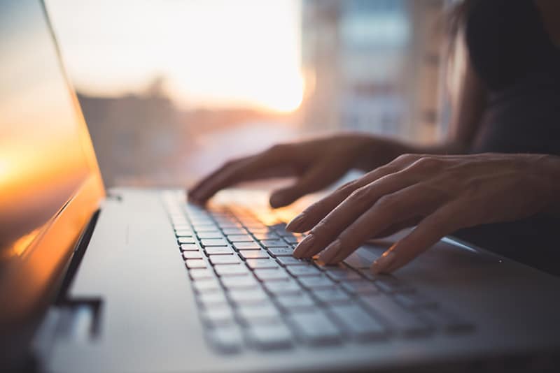 Woman typing on keyboard with sun reflecting off laptop screen