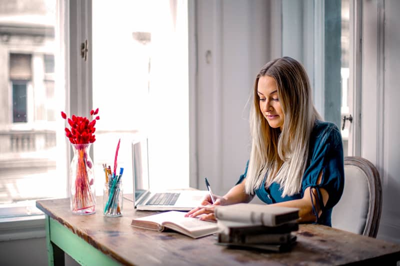 woman in long sleeved shirt sitting at a table working from home