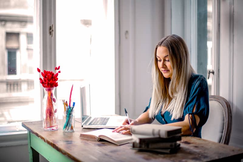 woman in long sleeved shirt sitting at a table working from home
