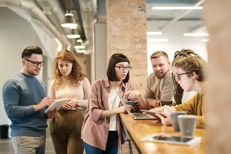 shallow focus photo of people having a discussion while looking at a laptop and having hot drinks.