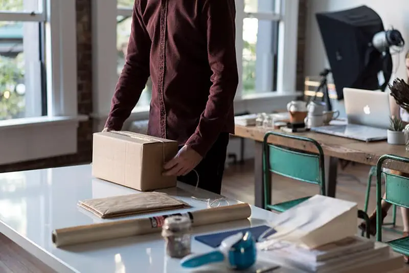 Person wrapping package on table for ecommerce store