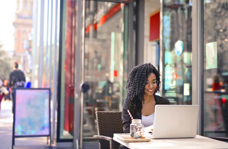 Millennial freelancer sitting on chair outside café working on laptop