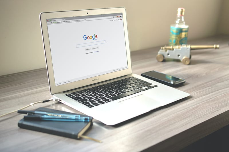 Google search engine on Macbook screen next to smartphone and notebook on desk