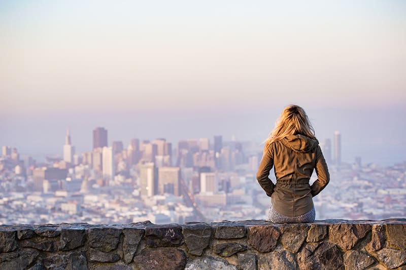 Woman on a rock wall looking out to urban environment - city