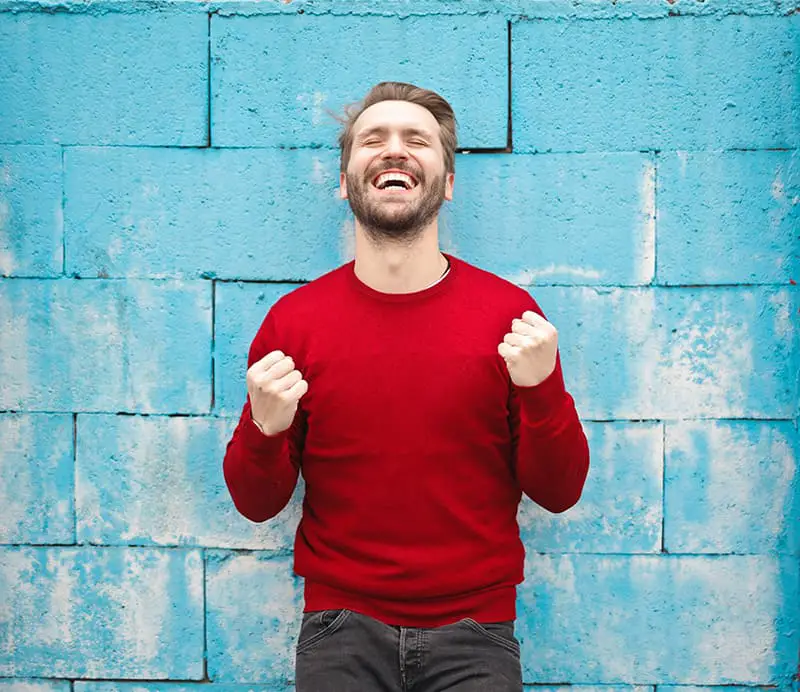 man wearing red long-sleeved t-shirt standing beside wall demonstrating personal power for success