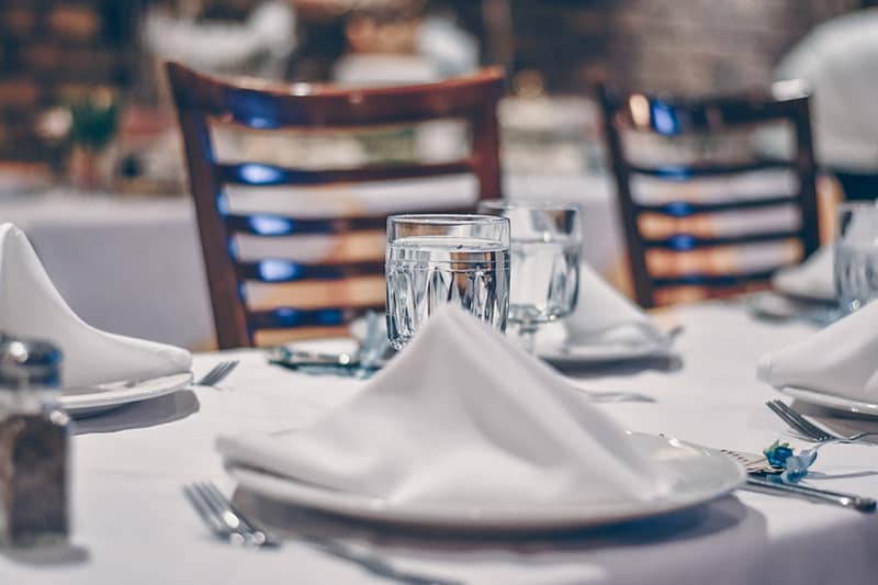 Depth of field photo of clear drinking glass on white table near plate in restaurant