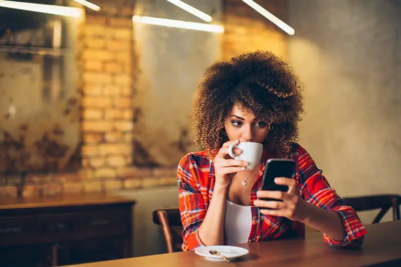 young woman looking at smartphone and having a drink