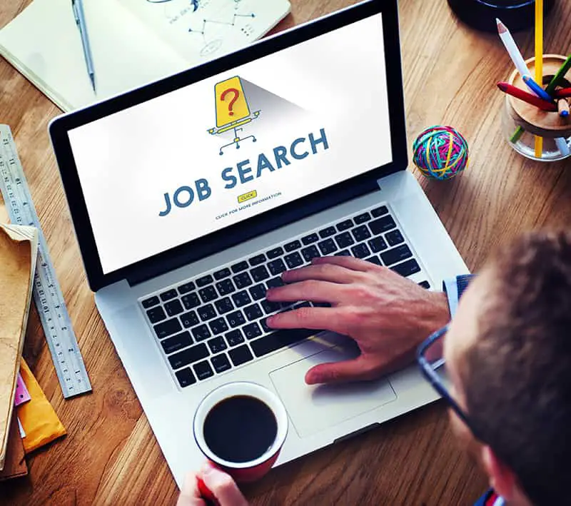 A man holding cup of coffe while browsing for job online in the laptop