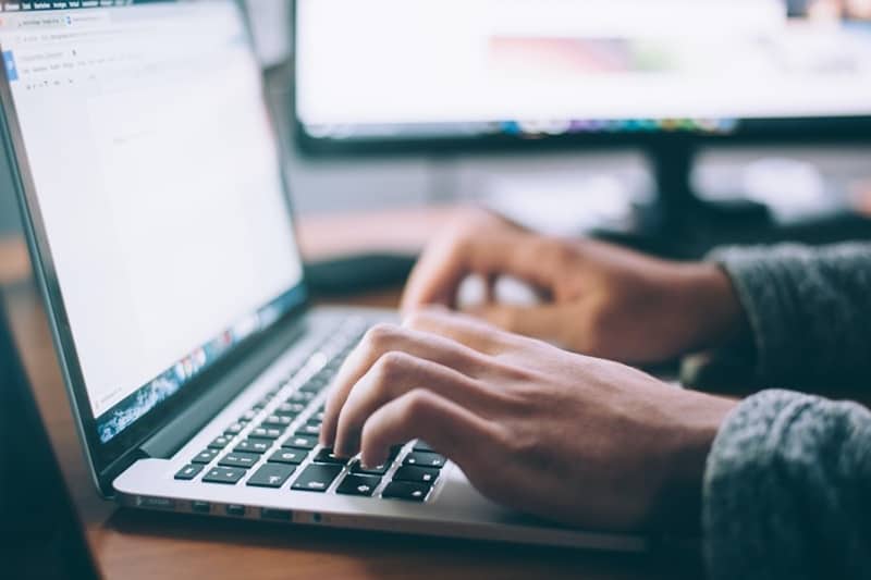 A hands of a person wearing long sleeves typing in laptop keyboard.