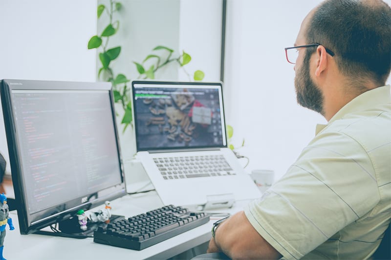 A man wearing eyeglasses facing in front of computer and laptop