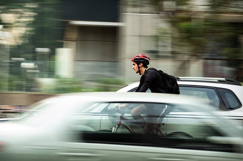 Man wearing a bike helmet and backpack on bicycle on road between cars