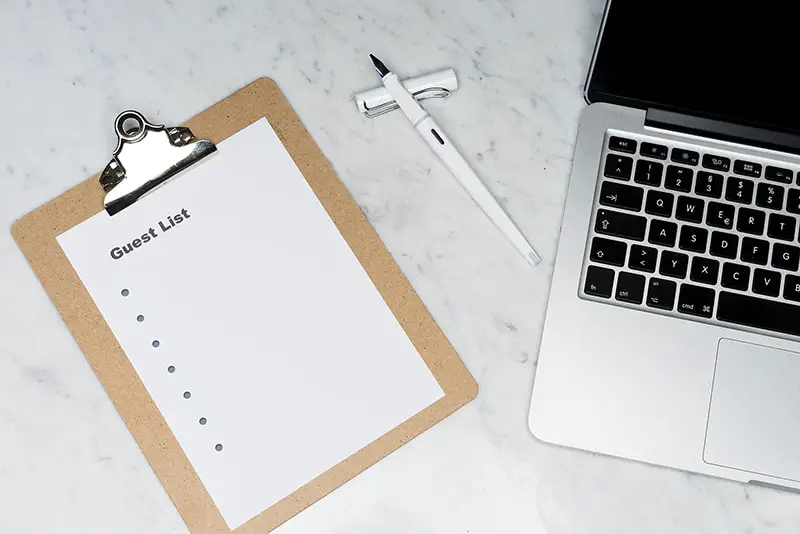 Paper saying guest list clipped onto a clipboard next to laptop