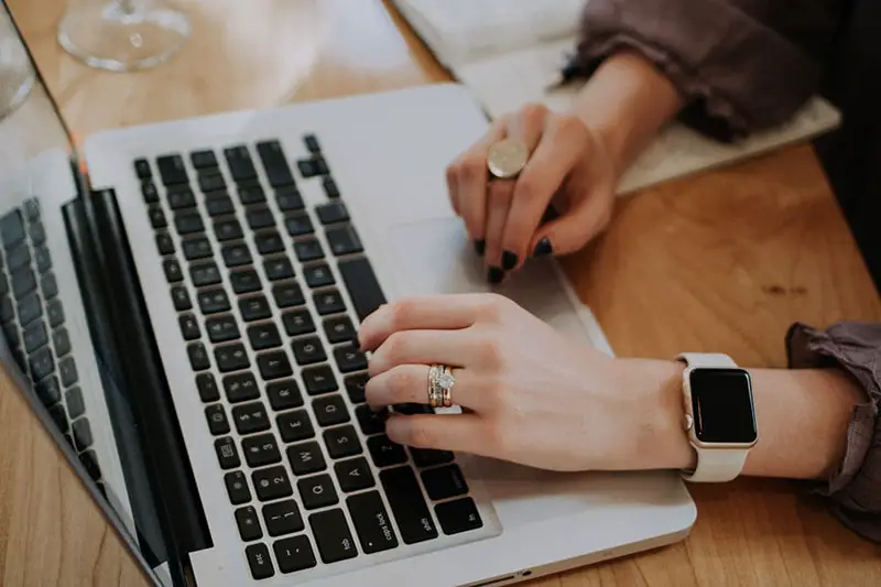 Hands of a woman with brown long sleeves typing in the laptop keyboard