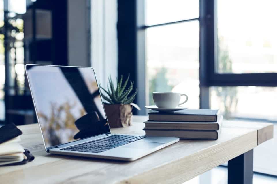 Open laptop and books on table in a room with lots of bright sunlight