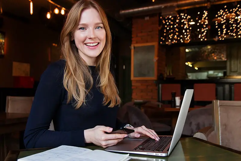 A young woman in fronrt of laptop while holding black smartphone