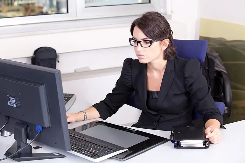 A business woman wearing eye glasses and black suits in front of computer