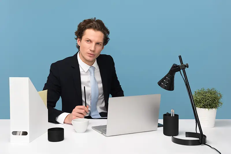 A businessman on his desk, wearing black suit in front of his laptop