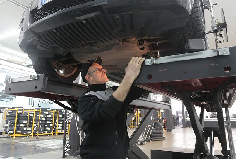 Man in black jacket working underneath a vehicle in car repair shop