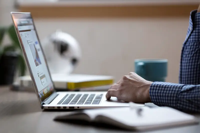 A person wearing blue checkered long sleeves typing in laptop keyboard