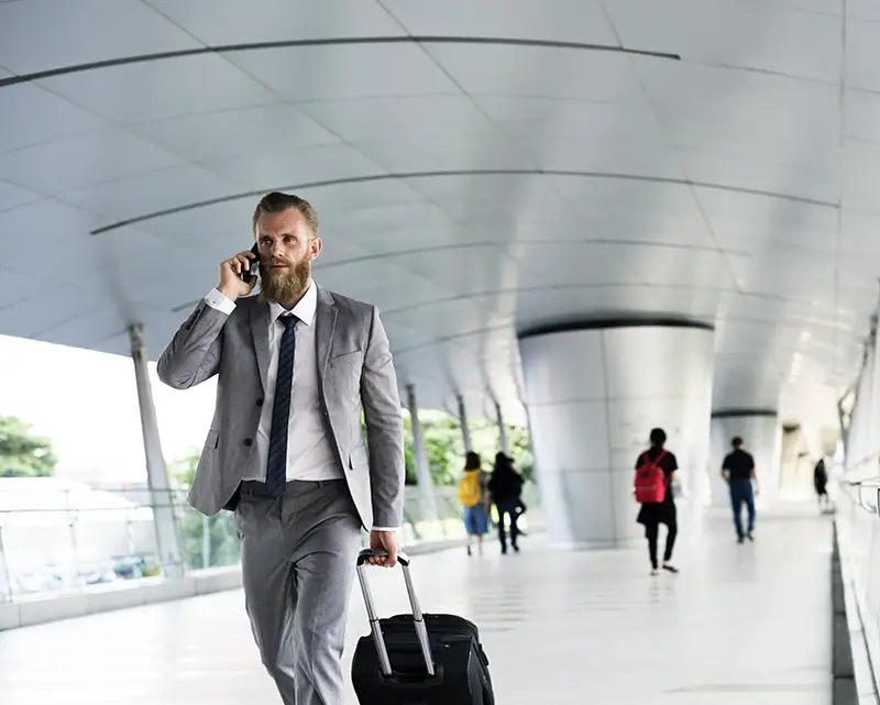 A business man pulling his luggage while calling on his mobile phone
