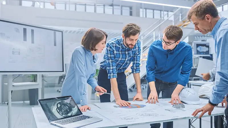 Group of Engineers and Technicians on a Meeting Gather Around Table with Engine Design Technical Drafts, Have Discussion, Analyse Technology