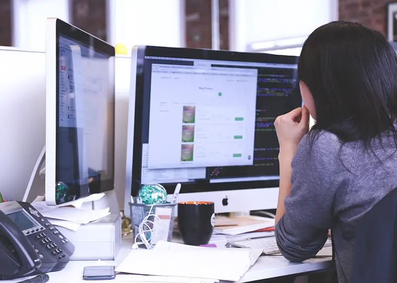 A woman in front of two computer monitor