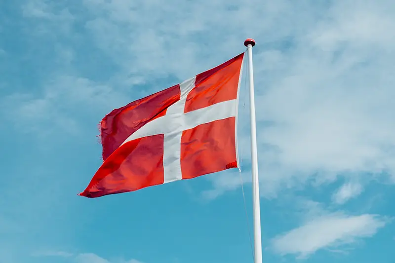 Danish Flag - red and white flag on flag pole - blue sky and clouds in background