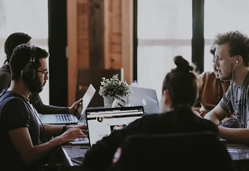 Team of people working around a table on laptop computers