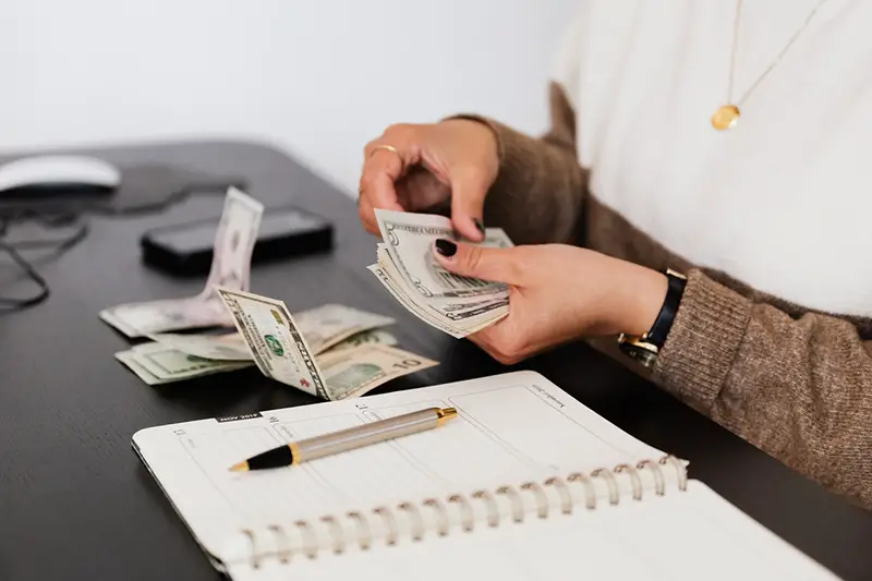 close crop image of person counting money – USA dollar bills - while sitting at a table