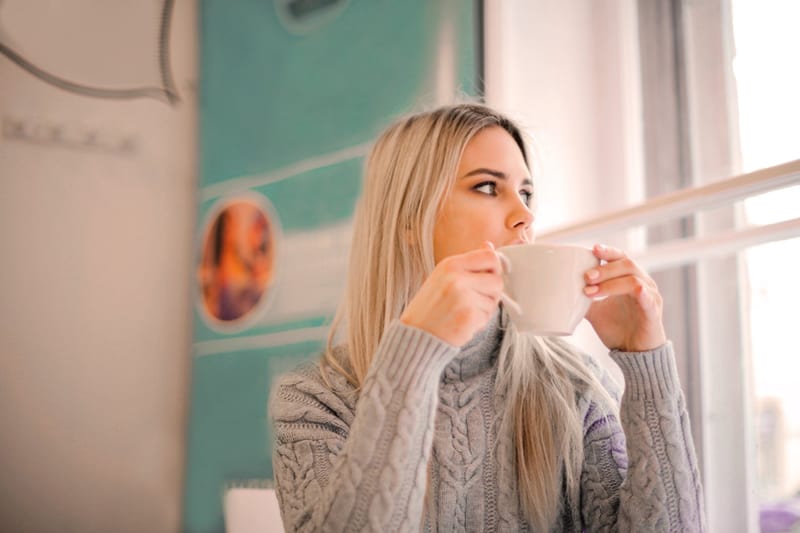 woman in gray sweater drinking from white ceramic mug look out of the window – have a break to be more productive 