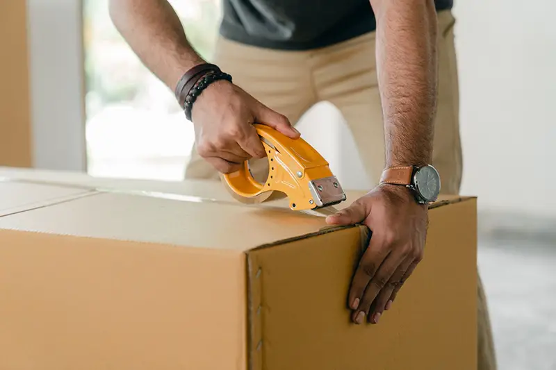 close cropped image of man taping carrying box with scotch tape – moving relocation
