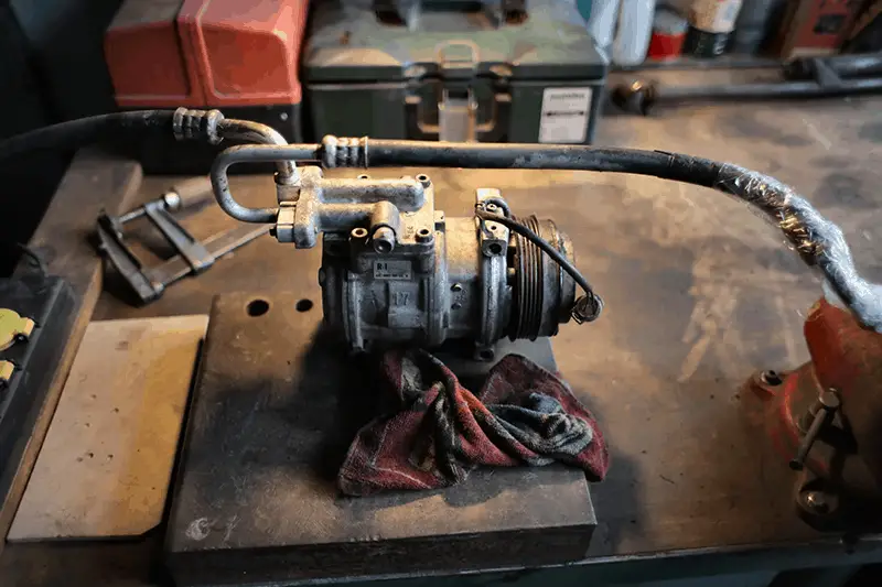 A metal air conditioning compressor on workbench in garage