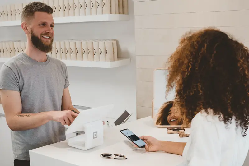 Smiling sales assistant servicing customer at POS in shop