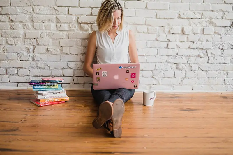 A young woman sitting in the floor while working on her pink laptop