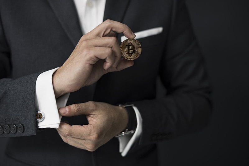 Man in dark suit and white shirt with cufflinks - holding a bitcoin cryptocurrency