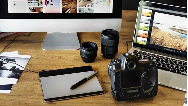 Camera and lenses on desk next to laptop computer and monior - photo editing 