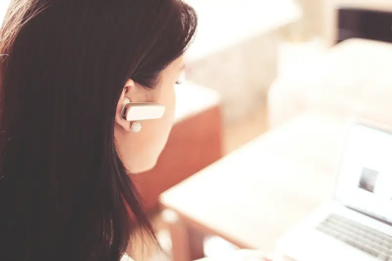 female customer support agent wearing earpiece and using a laptop