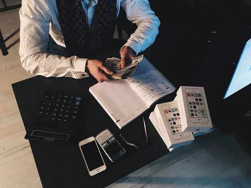 A person counting money with smartphones in front on desk