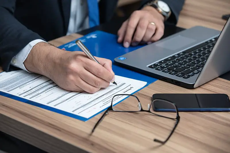 A lawyer writing in a paper while in the front of his laptop